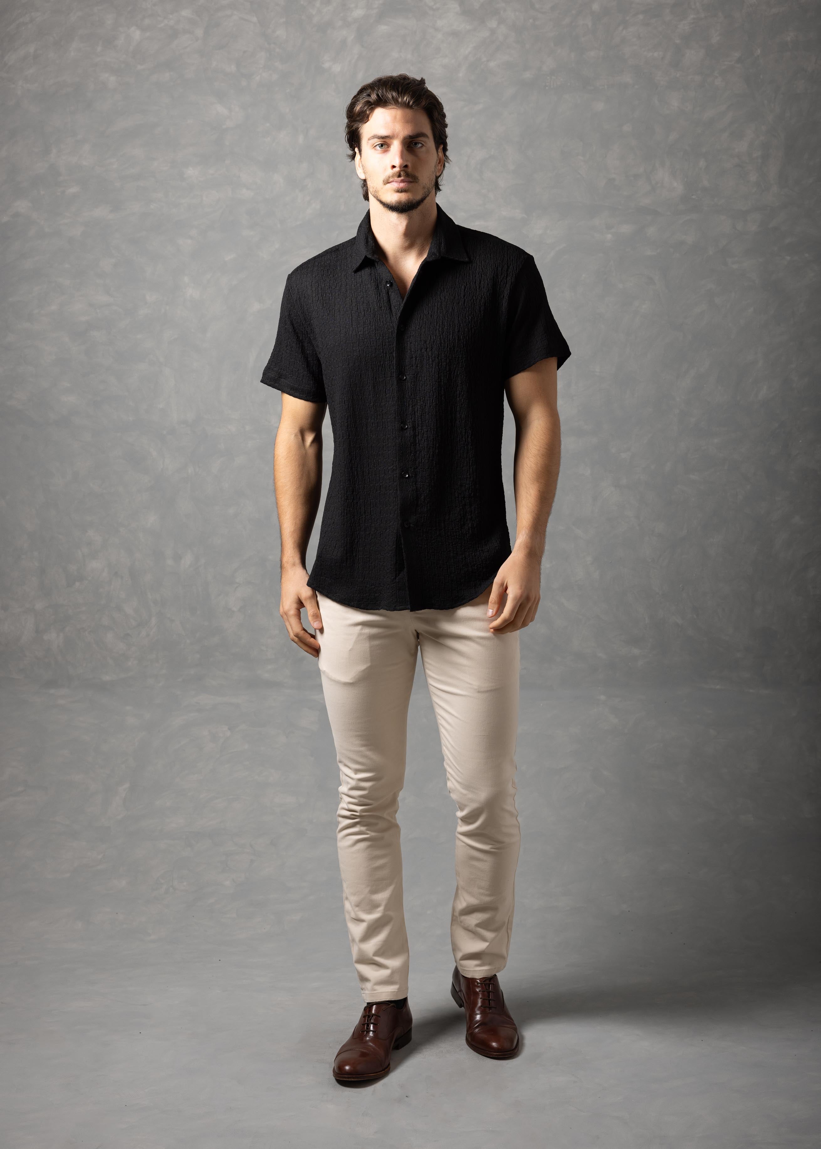 Man wearing a black shirt and beige pants against a gray background