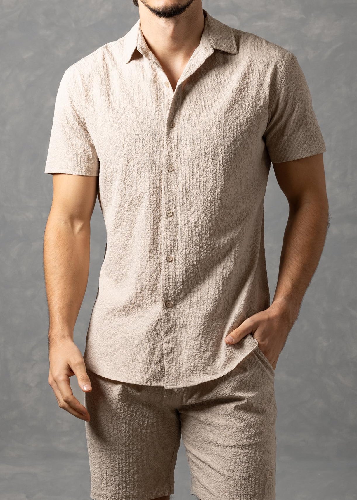 Man wearing a beige linen shirt and shorts against a gray background