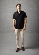 Man wearing a black shirt and beige pants against a gray background