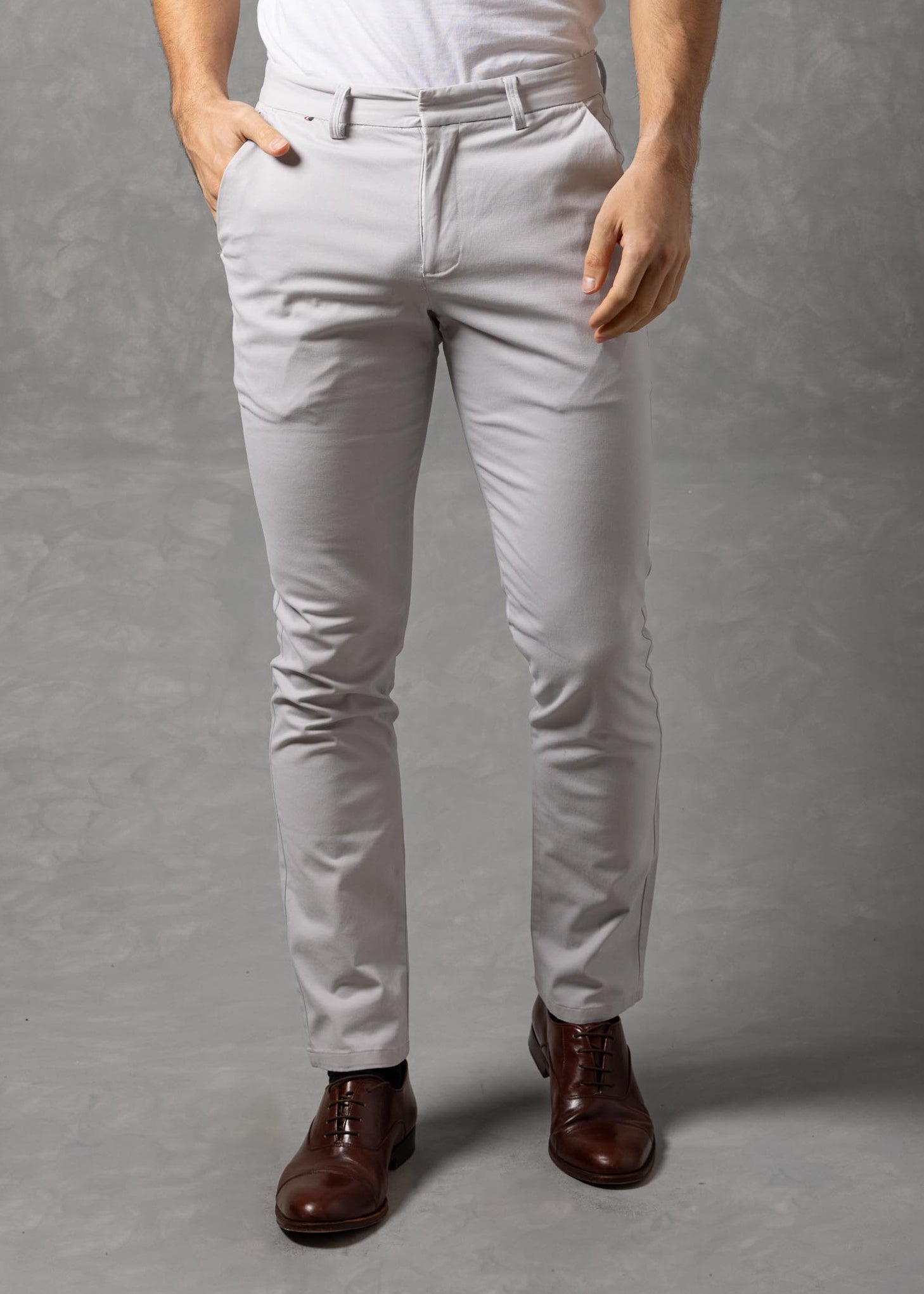 Man wearing a white t-shirt and light gray pants against a gray background