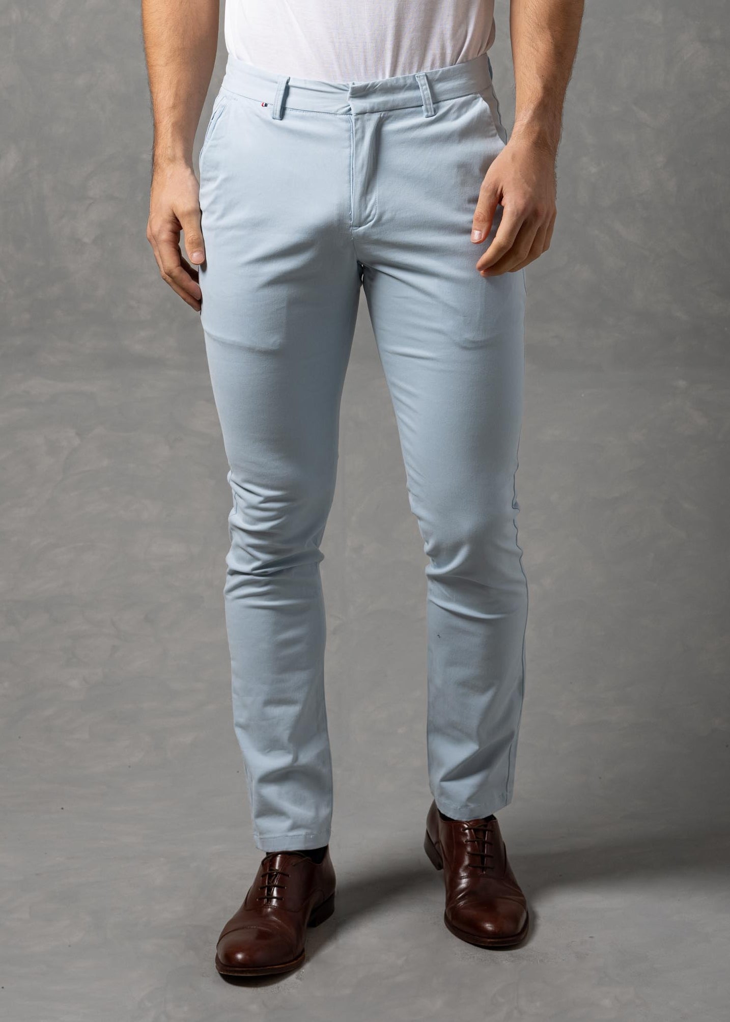 Man wearing a white t-shirt and light blue chino pants against a gray background