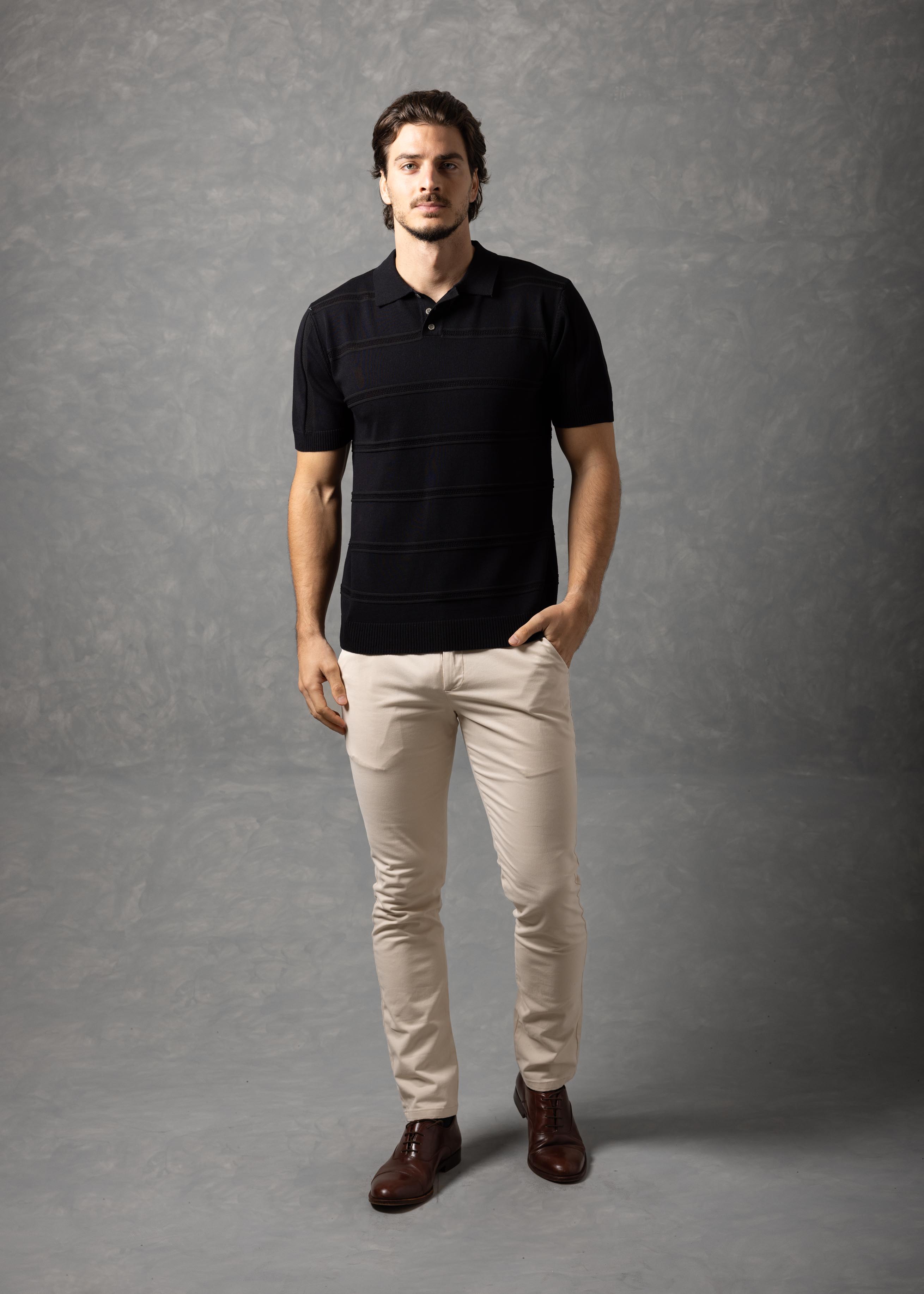 Man wearing a black polo shirt and beige pants against a gray background