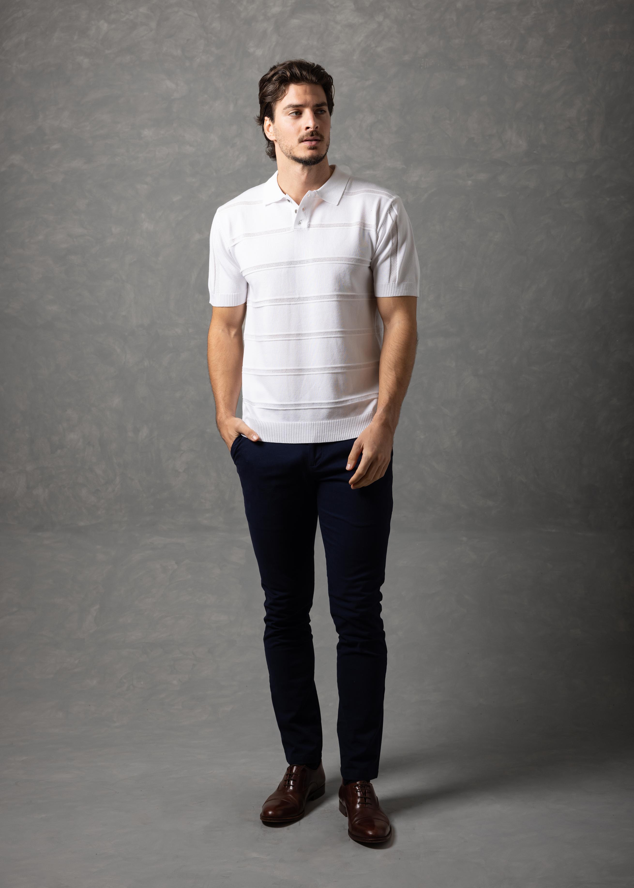 Man wearing a white striped polo shirt and dark pants against a gray background