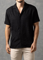 Man wearing a black shirt and beige pants against a gray background