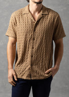 Man wearing a brown textured shirt and dark pants against a gray background