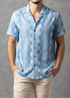 Man wearing a light blue patterned shirt and beige pants against a gray background